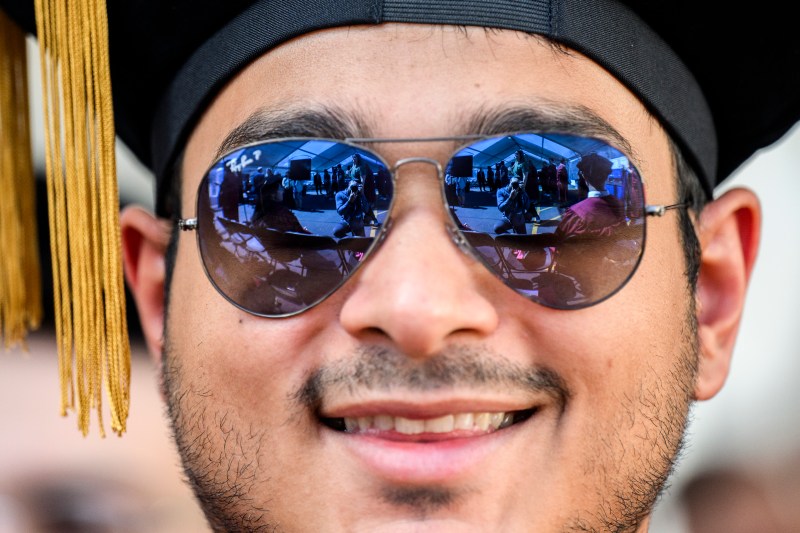 A student smiling wearing a grad cap and Ray Ban sunglasses.