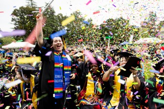 A graduate waving and cheering as confetti falls around them at the Oakland Commencement ceremony.