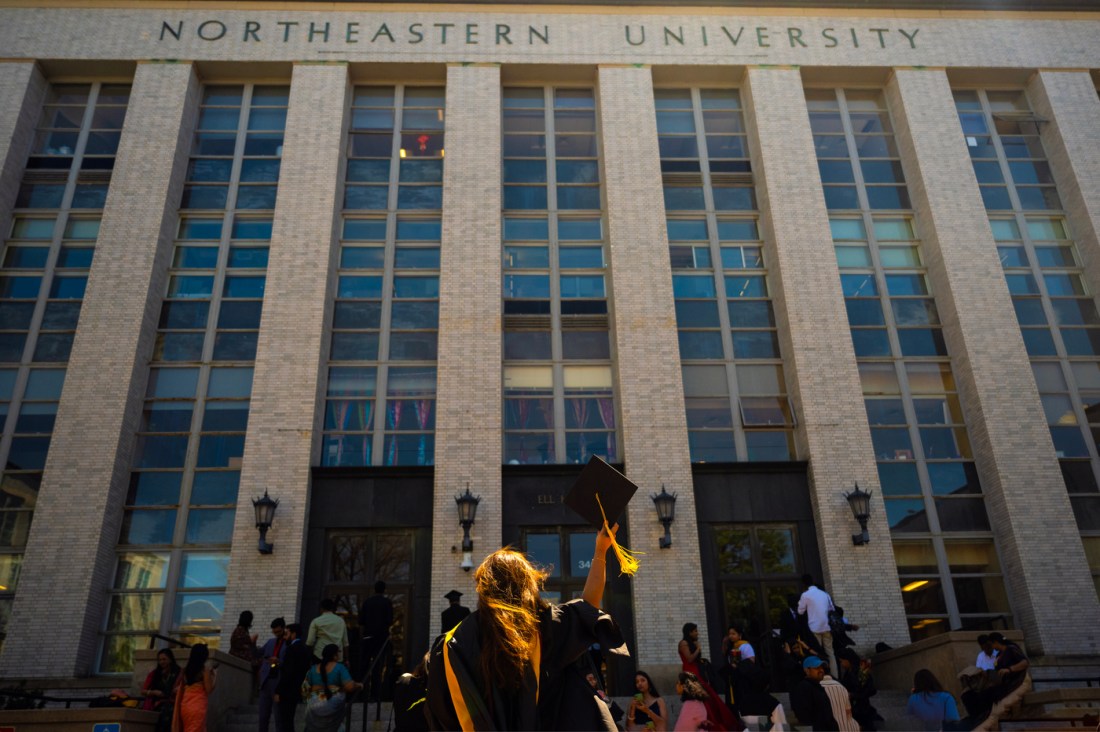 A graduate posing with with their back turned to the camera in front of Ell Hall.