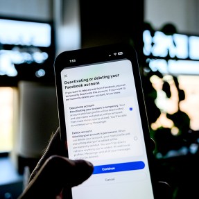 A person's hand holding up an iPhone ready to press the 'deactivate' button on Facebook with their thumb.