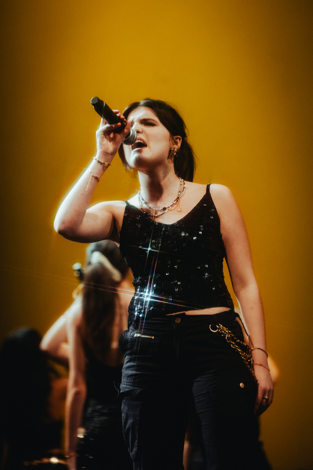 A singer from Pitch Perfect A Capella singing into a microphone.