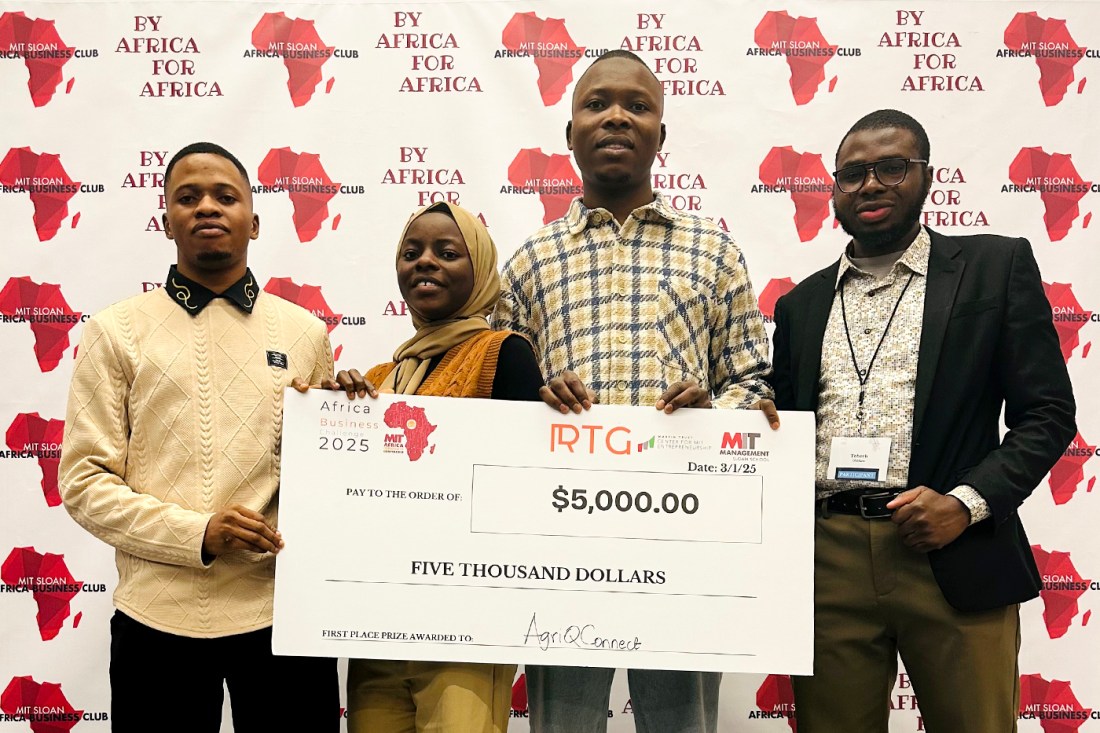 A group of four students posing in front of a photo backdrop while holding a check for five thousand dollars.