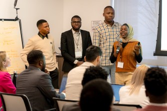 Four students standing at the front of a crowded room presenting on their app.