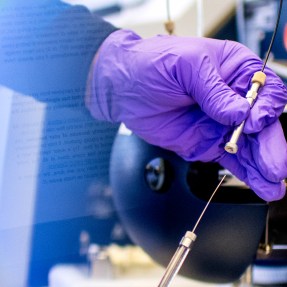 Jeffrey Agar's hand in a purple glove holding a piece of lab equipment.