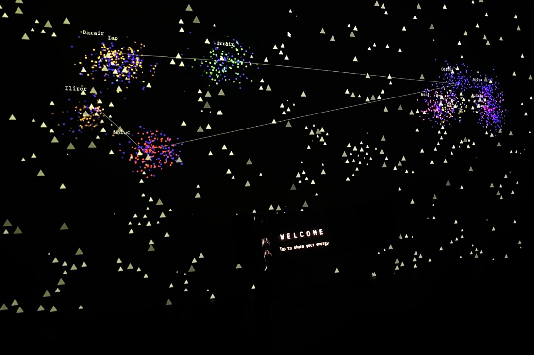 An exhibit on a screen showing a dark background with small yellow triangles and other shapes mapped on to it.