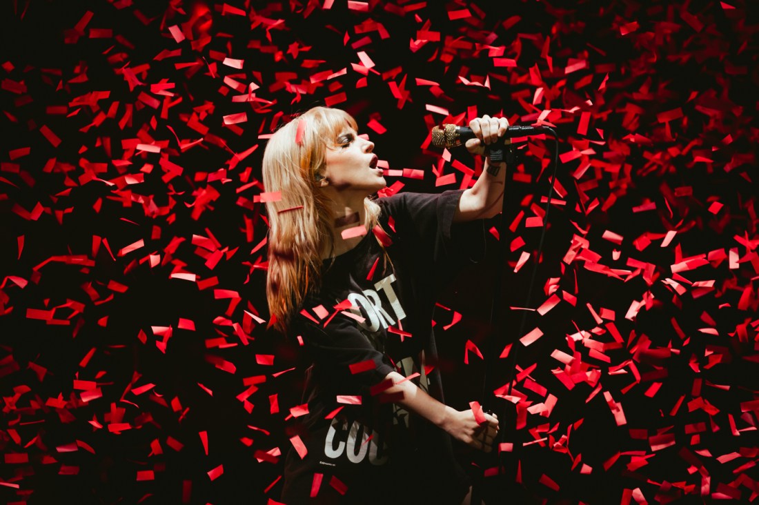 A concert photo of a singer performs mid-verse as red confetti rains down around her.