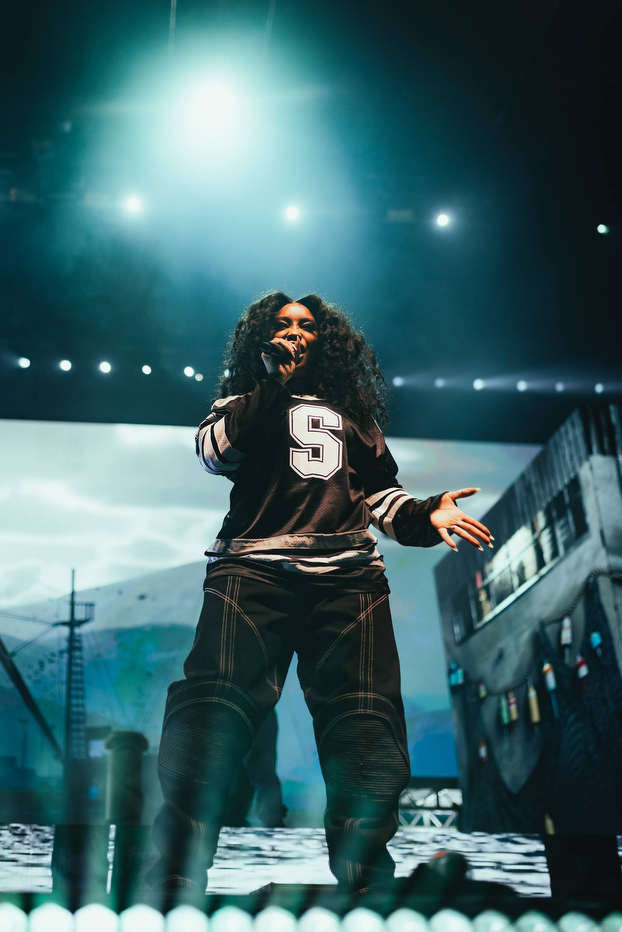 SZA sings on stage in front of a cityscape backdrop.
