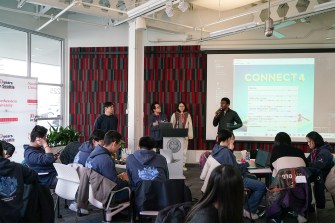 Students presenting AI tools at the front of a classroom at a hackathon.