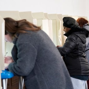 Three people marking their ballot while voting.