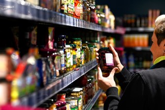 A person holding a jar of olives off of the shelf at a grocery store.