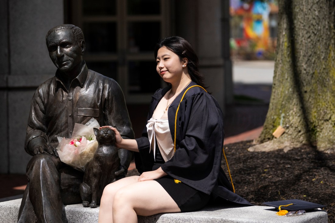 A Northeastern graduate posing next to a statue of Robert Shillman and his cat.