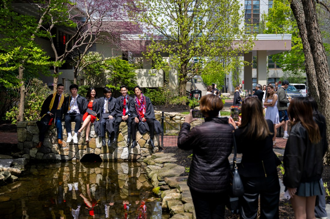A group of graduates sitting on a stone bridge over a koi pond.