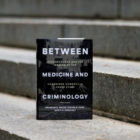 The book "Between Medicine and Criminology" stands upright on outdoor stone steps.