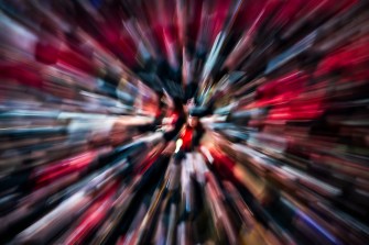 A radial blur effect creates a zoomed motion look around a central graduate in red at a commencement ceremony.