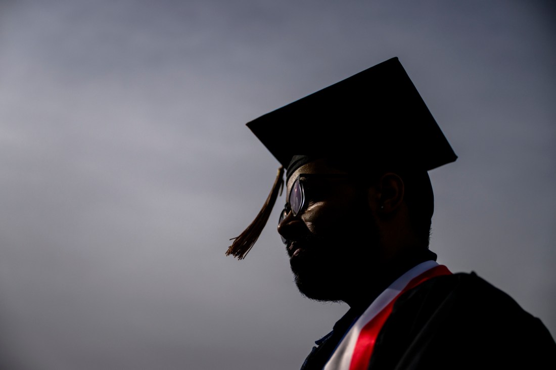 A graduate in cap and gown at a commencement ceremony, seen in silhouette.