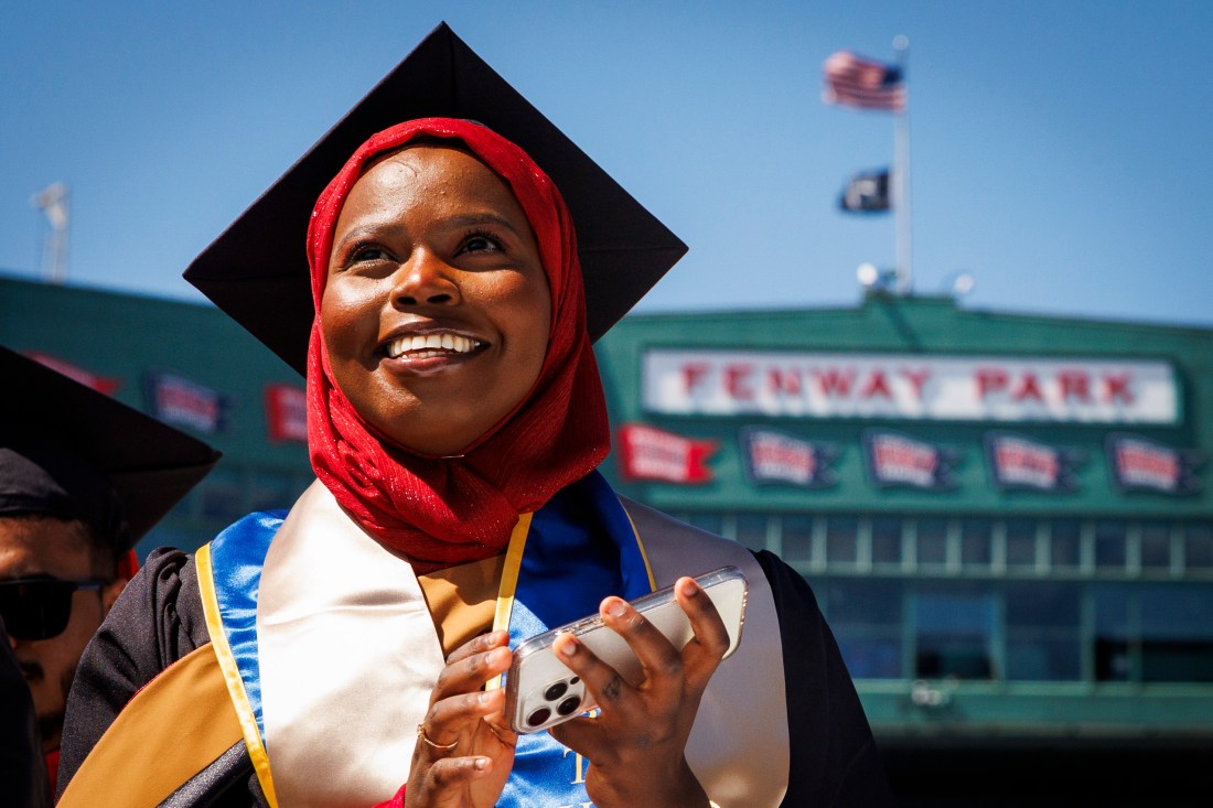 Graduate smiles while holding a phone at Fenway Park during Northeastern’s 2025 Commencement.