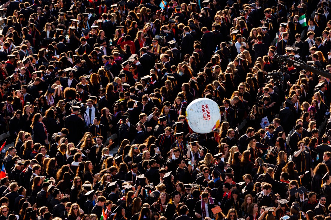 A large crowd of Northeastern graduates gathers on the field at Fenway Park, with a “Huskies for Life” beach ball in the air.