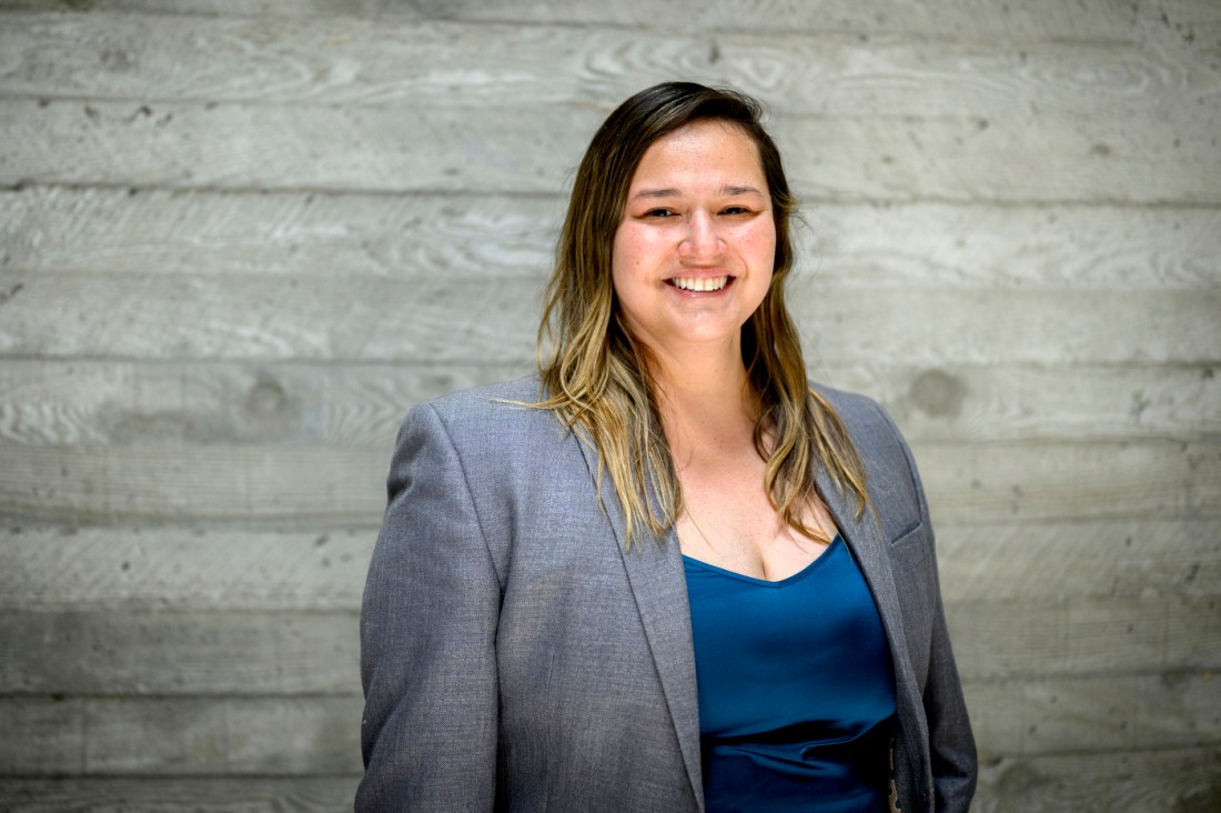 Portrait of Jay Nakhai wearing a grey blazer in front of a wooden panel background.
