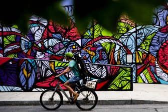 A person riding their bike in front of a colorful geometric mural on a wall outside.