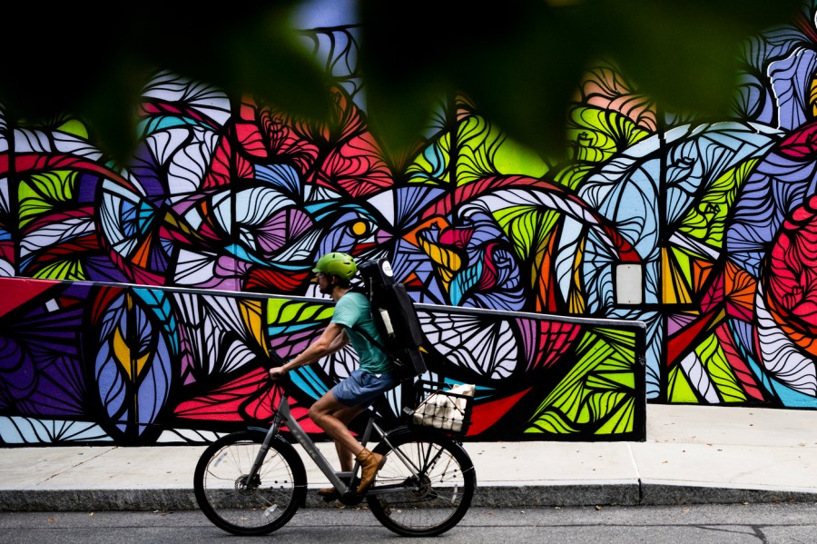 A person riding their bike in front of a colorful geometric mural on a wall outside.