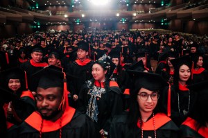Rows of Northeastern graduates wearing black caps and gowns with red accents seated inside of Benaroya Hall for the Seattle Campus Commencement Ceremony.