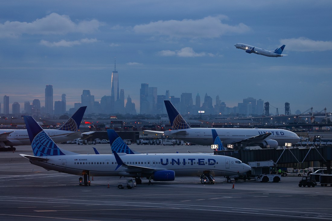 Airplanes on a runway with a city skyline in the background.