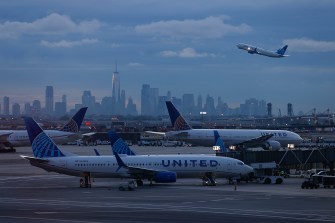 Airplanes on a runway with a city skyline in the background.