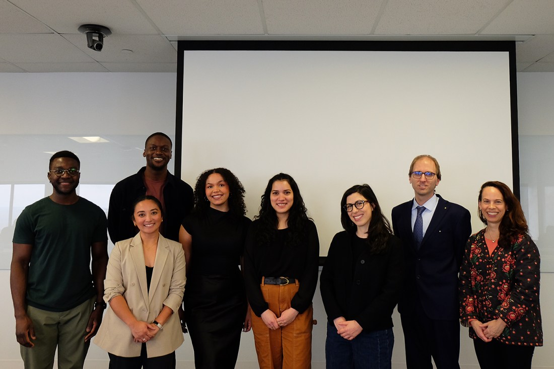 A group of eight people posing for a photo inside of a classroom. In the background is a projector screen.
