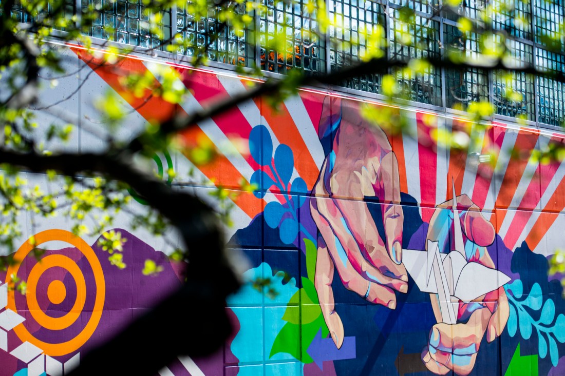 The "999 Cranes" mural. Many colorful, graphic elements behind two hands folding an origami crane.
