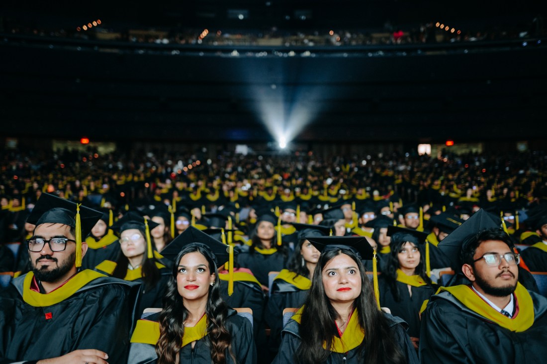 A wide shot of rows of graduates wearing black and yellow commencement regalia sitting in Meridian Hall for the Toronto graduation.