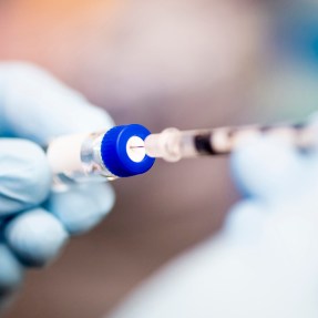 A person filling a syringe with gloved hands.
