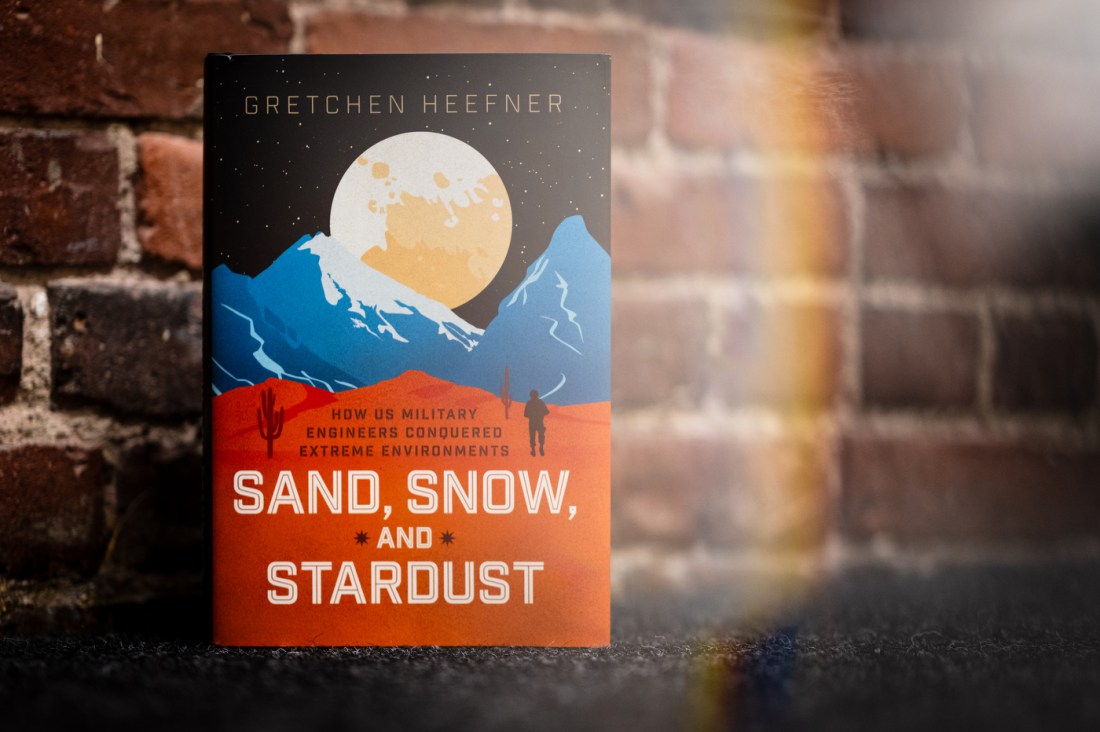 A photo of the author's book, "Sand, Snow, and Stardust," against a brick wall.