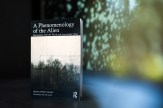 Book cover of &#039;A Phenomenology of the Alien&#039; in front of an atmospheric, blurred landscape with trees.