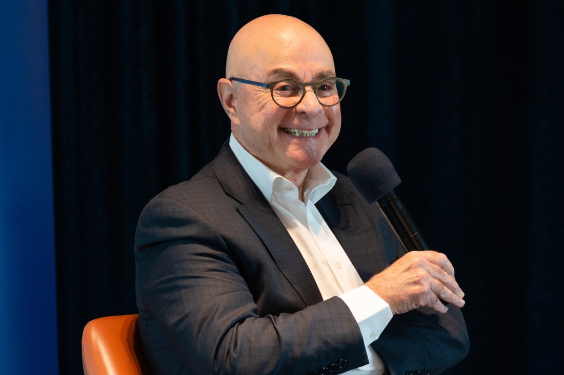 President Aoun holding a microphone and smiling while sitting in an orange chair at the AI Synergy Summit.