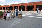 A group of people walking, some moving mobile carts, outside a brick building with &quot;COMMISSARY&quot; spelled out in large white letters across the top