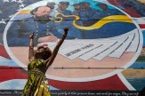 A woman raises her arms in front of a colorful mural during a Juneteenth celebration.