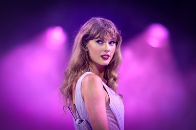 Taylor Swift performs on stage under purple lights, glancing over her shoulder during a concert.