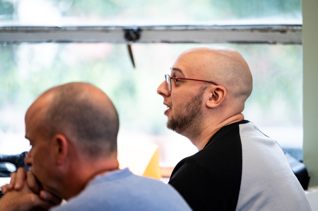 A person wearing a black and grey shirt and glasses talking at an AI integration workshop.