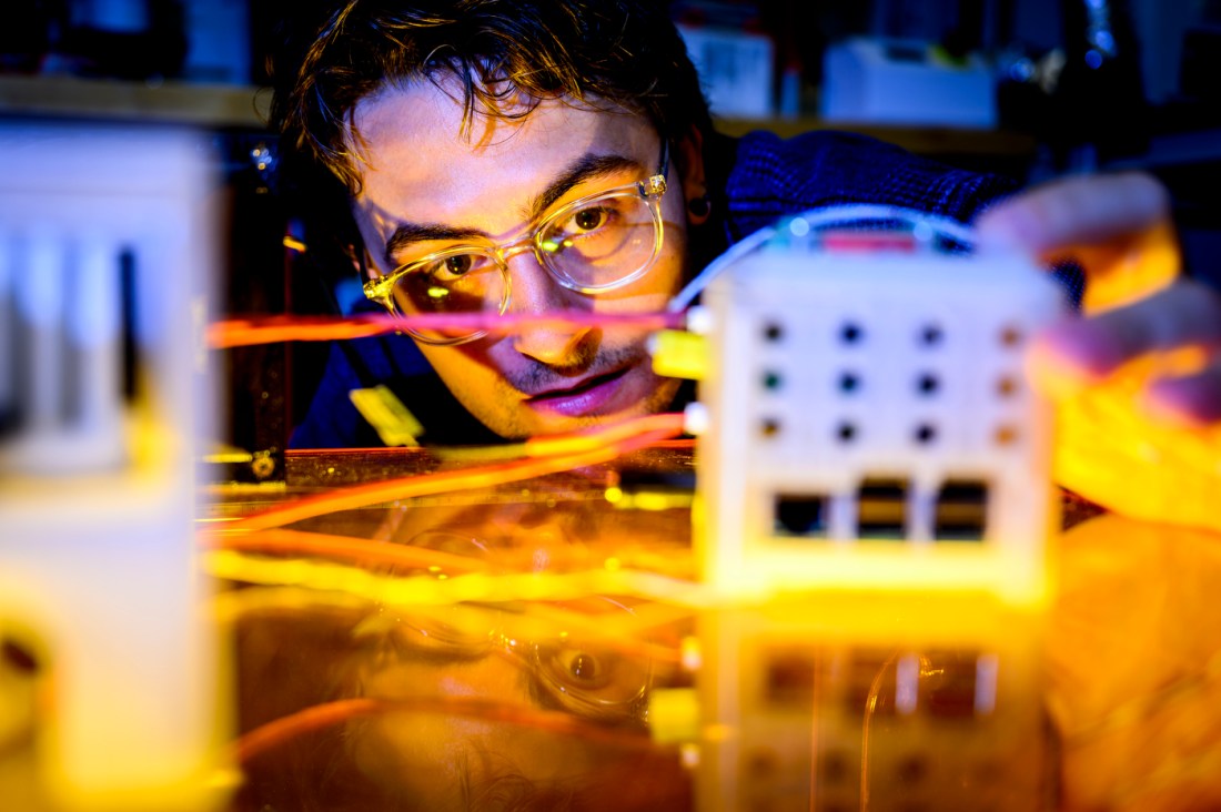Daniel Braconnier wearing safety glasses examines heat-conductive plastic composite material in laboratory with colorful lighting and equipment in background.