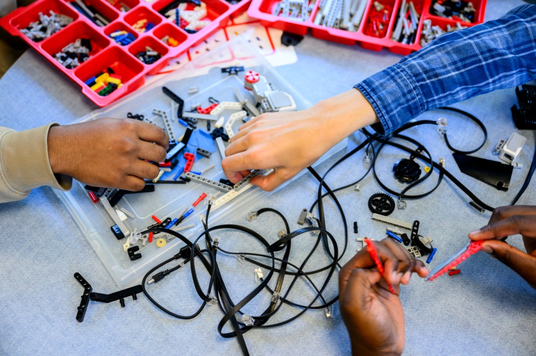 Two hands grab LEGO parts as another works on assembly