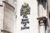 The exterior of a court building with a royal court of arms and &#039;The Royal Courts of Justice&#039; on it.