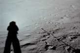 A shadow of an astronaut on the surface of the moon, with indents seen in the surface as well.