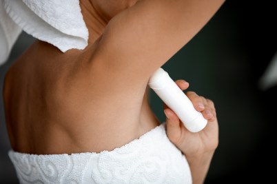 The side view of a woman, wrapped in a towel, applying deodorant.
