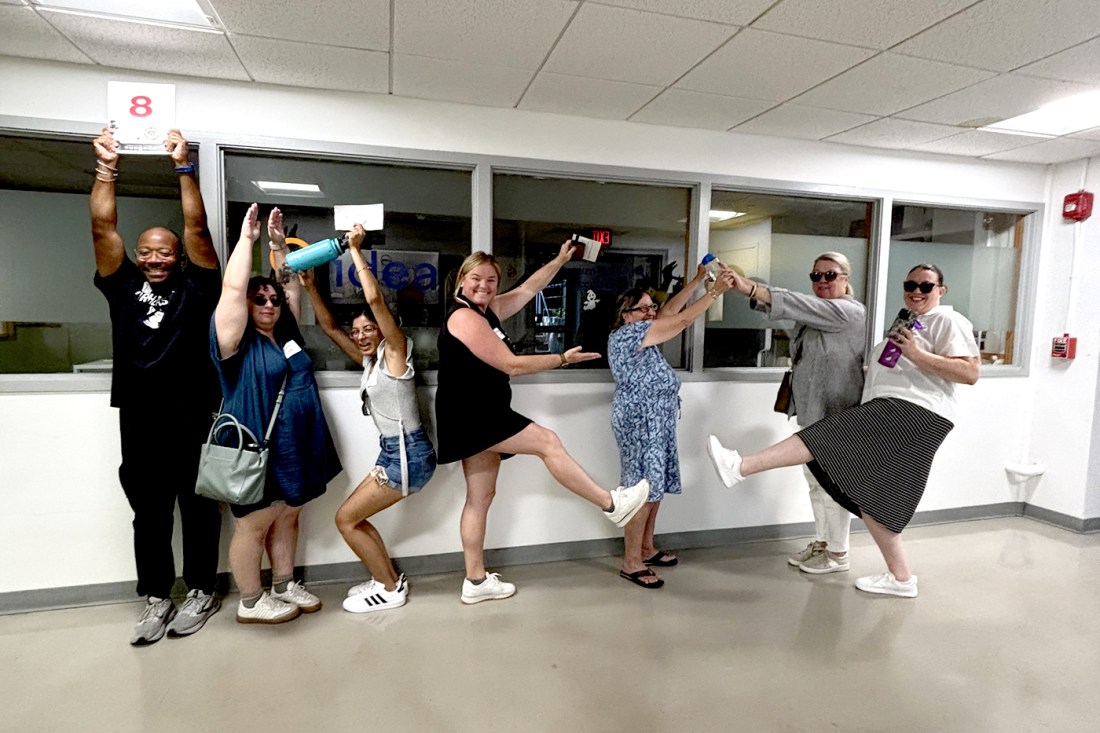 People posing to spell out IDEA. Everyone is in a white hallway and smiling.
