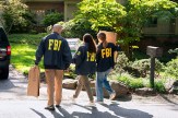 FBI agents shown carrying boxes in front of a residence in broad daylight.
