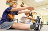 Several students sitting on the ground reaching for their toes as part of a fitness program.