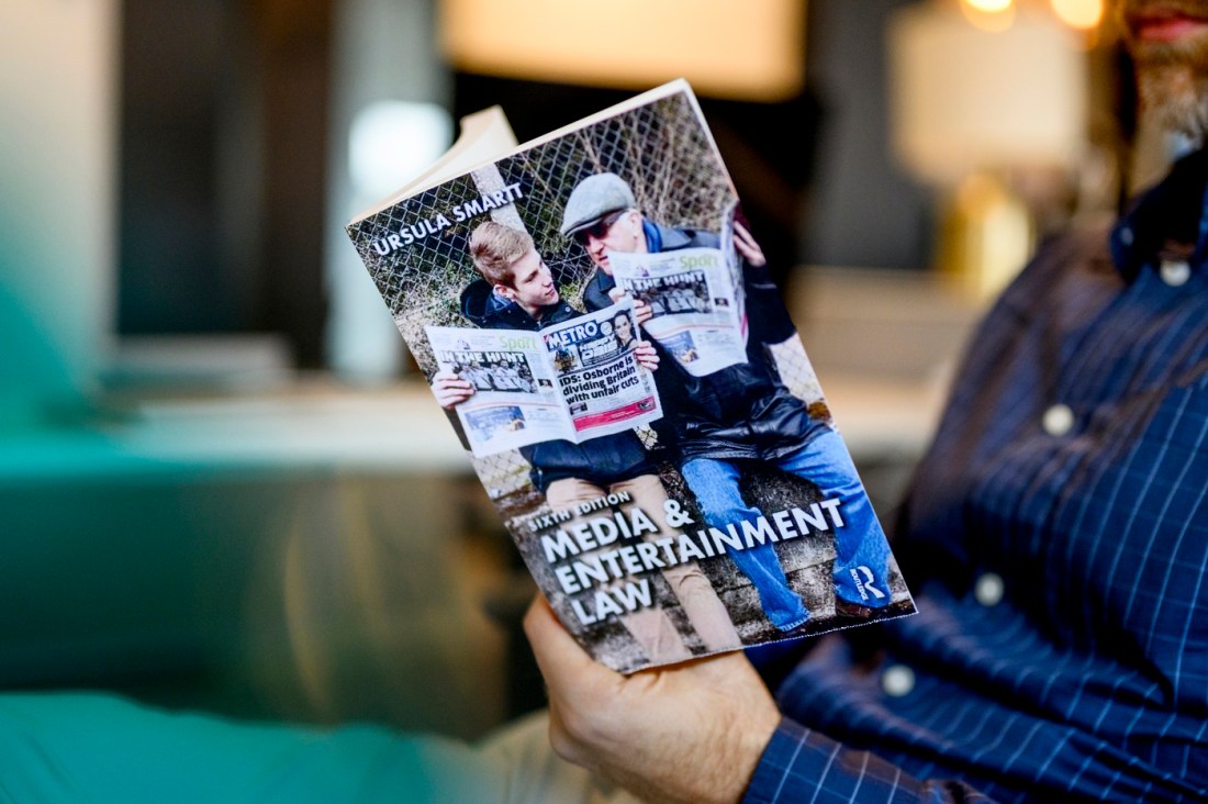 A person holds wearing a blue button-up shirt, his face out of view, holds open a book.