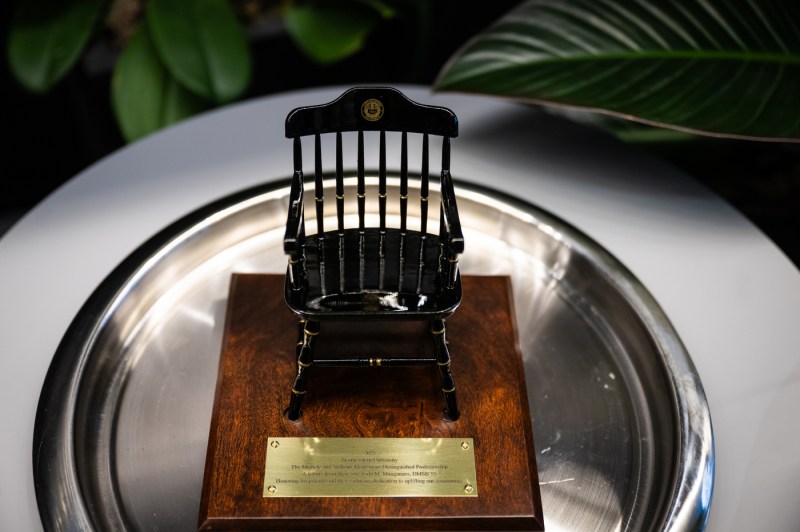 A close-up of the Michele and Anthony Manganaro Distinguished Professor plaque, which is wooden with a chair on it.