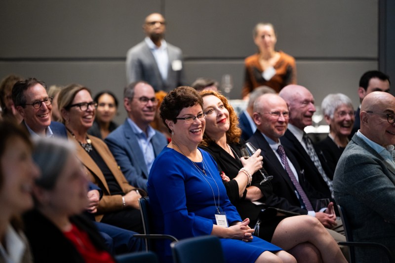 Members of the audience laugh.