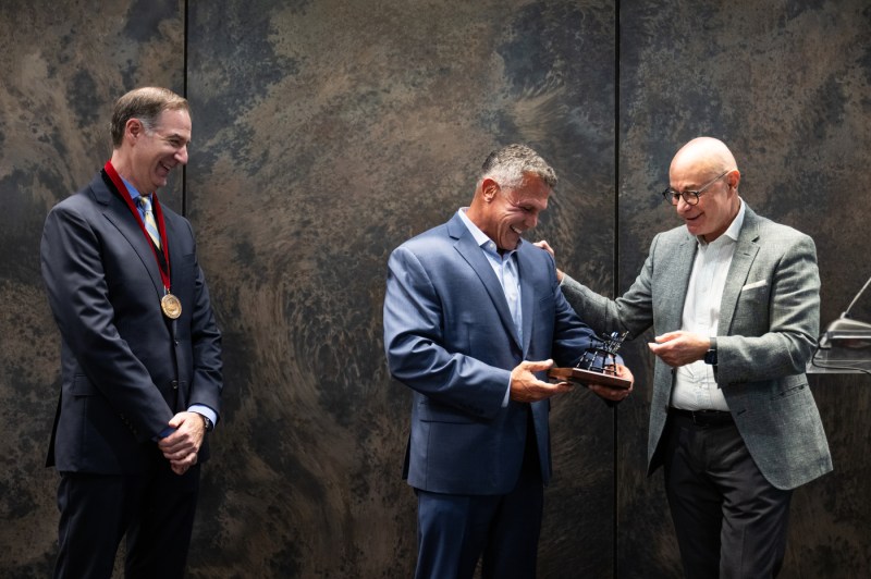 Todd Manganaro, smiling, looks at the distinguished professor plaque with President Aoun and Charles Hillman, who is wearing his medallion.